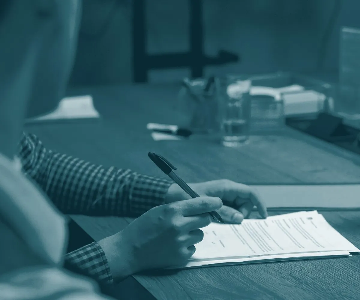 Mãos revisando um contrato com caneta sobre a mesa de reunião