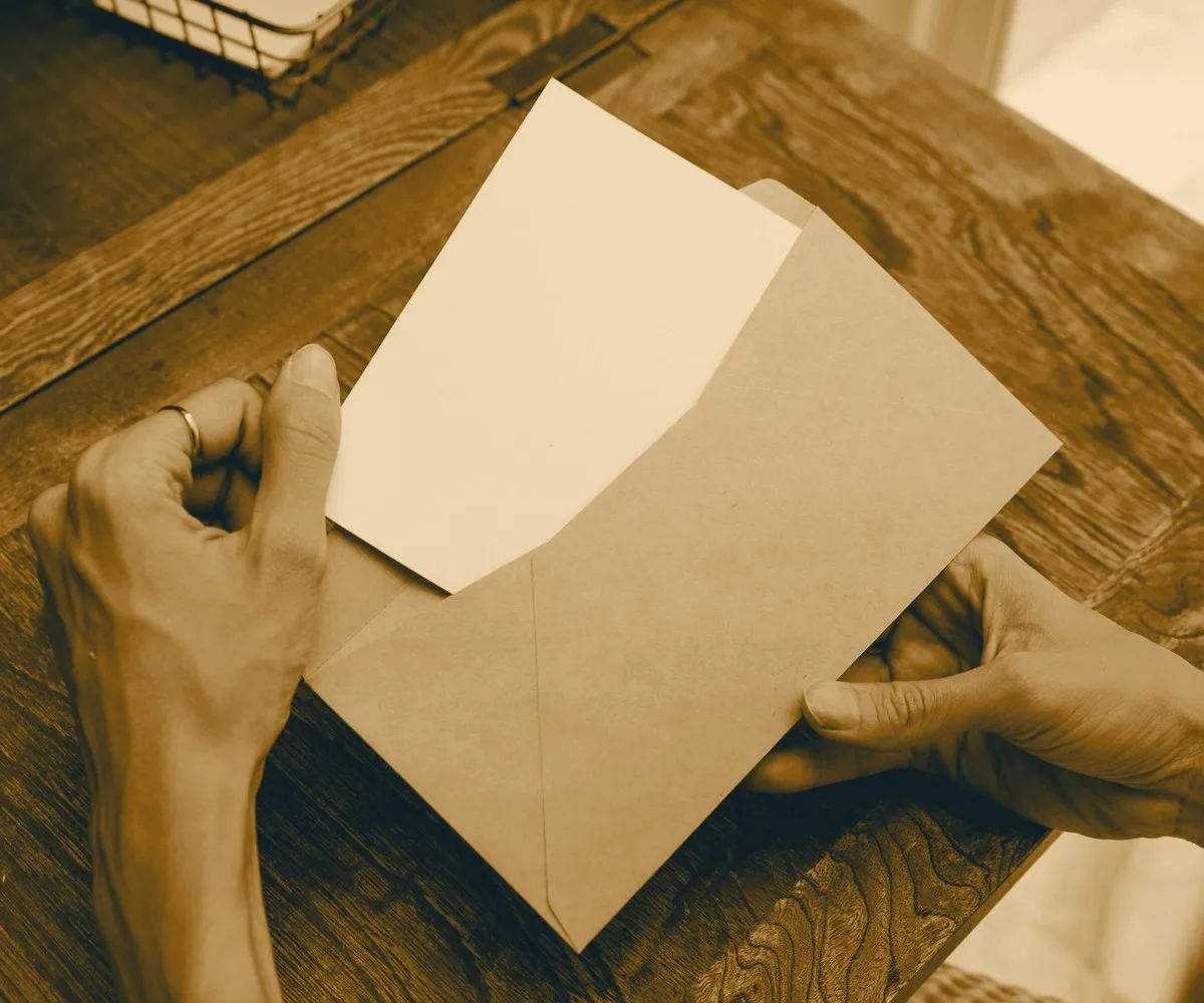 Mãos retirando uma folha de um envelope pardo sobre uma mesa de madeira